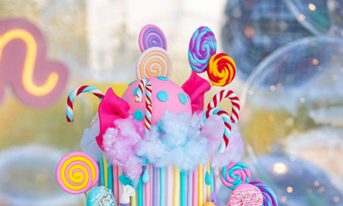 Whimsical pastel cake decorated with oversized lollipops and cotton candy accents.
