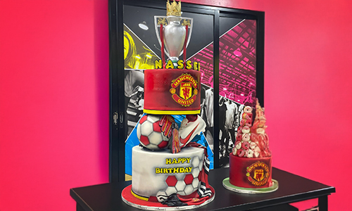 Manchester United-inspired birthday cake with sneakers, trophy and team-themed decorations.